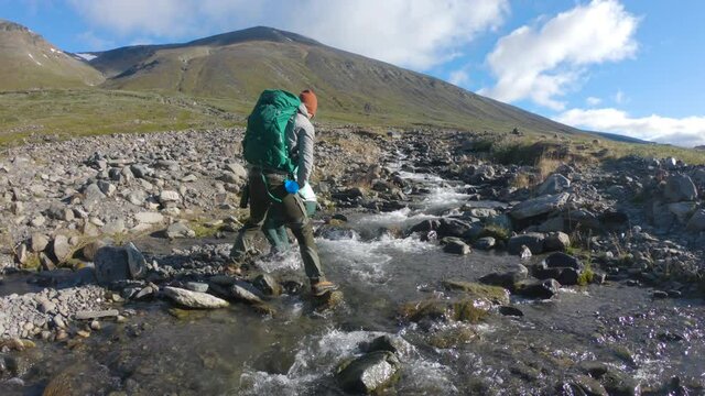 Male hiker helping his girlfriend over a rocky stream in the nature. Together on a journey towards the big mountain, Kebnekaise, Northern Sweden.