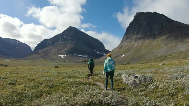 Male and female hiker walking on an offroad trail in the swedish nature. You can see two big mountains in the background.