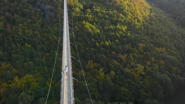 Aerial shot of young woman walking across Geierlay suspension bridge in Western Germany.