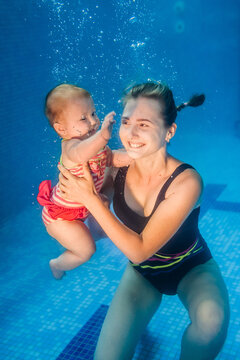Mother holds baby, daughter learn to swim on swimming lesson, doing physical exercises, dive underwater with in pool. Healthy lifestyle, active parents. Enjoy of swimming and bubbles.