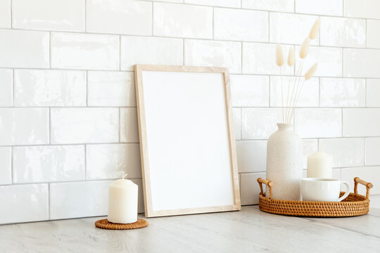 Blank picture frame mockup, rattan tray with cup of coffee, vase of dried flowers, candles. Brick tiles wall on background. Modern Scandinavian style interior.