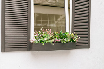 White wall of the house outside. The window is open for ventilation. Wooden shutters made of planks. Decorations from flowers.
