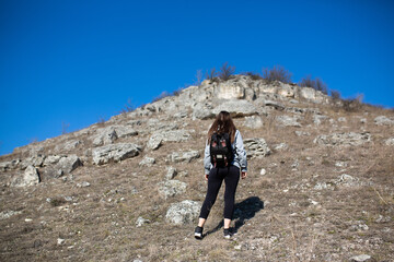Obraz na płótnie Canvas Traveling woman hiking with backpack climbs steep rocky terrain with blue sky on the background.