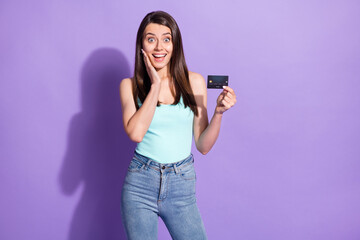 Photo of amazed charming young woman hold hands cheekbone debit card isolated on violet color background