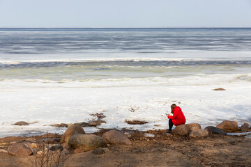 Russia. Saint-Petersburg. The girl is sitting on the shore of the pond. Ice on the Gulf of Finland.