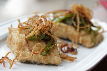 Cod fish, fried bacalao with onion, on white plate, wooden table in nature traditional dish of Spain, roasted meal, sidreria side dish in Basque country 