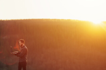 Fototapeta premium Man working outdoors with laptop in high mountains at sunset. He combines rest with work.