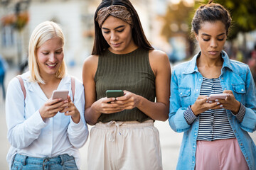 Fototapeta premium Three woman on the street using mobile phone.