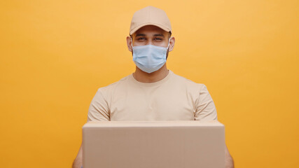 Courier with face mask holding cardboard box. Delivery of goods during coronavirus outbreak. High quality photo