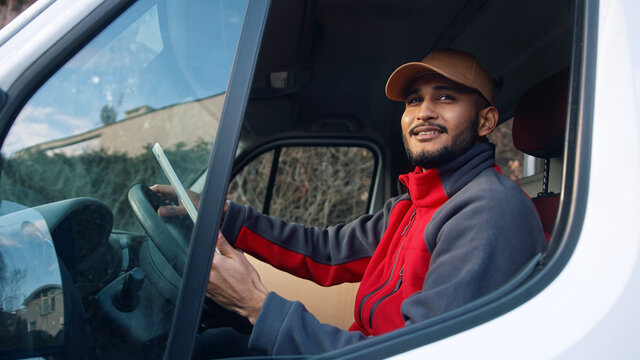 Happy indian courier using tablet in the van . High quality photo