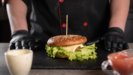 step by step recipe. Stage 9. The chef prepares a delicious burger. Close-up of hands in black gloves near the finished product, menu, delicious and unhealthy food.