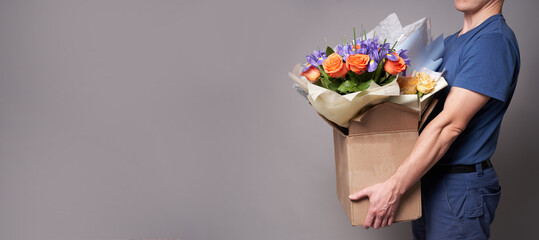 White male courier holding large cardboard box with several bouquets. Delivery concept. Man in blue shirt. Quality banner with deliveryman. Copy space