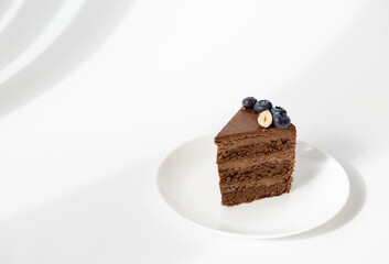 A slice of chocolate cake with blueberries and nuts on a white plate. Sugar, gluten and lactose free.