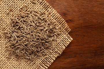 Macro close-up of Organic cumin seed (Cuminum cyminum) or jeera on the wooden top background and jute mat. Pile of Indian Aromatic Spice. Top view