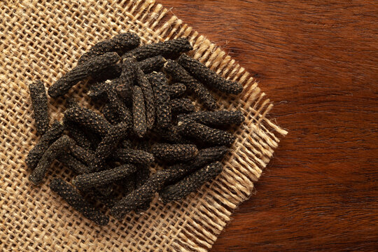 Macro close-up of Organic Indian long pepper  (Piper retrofractum ) on the wooden top background and jute mat. Pile of Indian Aromatic Spice. Top view