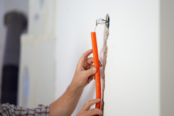 Workers hands positioning orange corrugated tube into a hole in a wall