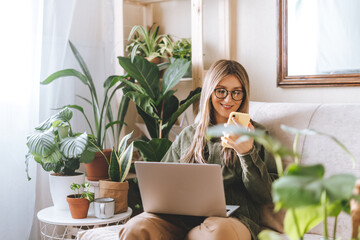 Freelance woman in glasses with mobile phone typing at laptop and working from home office. Happy...