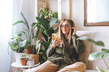 Freelance woman in glasses with mobile phone listening music in headphones and relax at home. Happy...