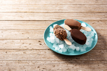 Chocolate popsicles and crushed ice on blue plate on wooden table. Copy space