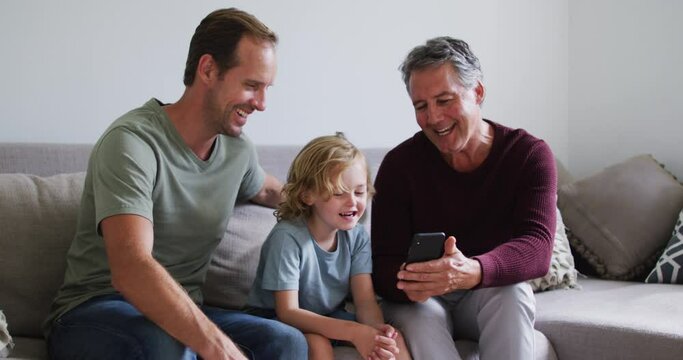 Caucasian grandfather, father and son smiling while using smartphone together at home