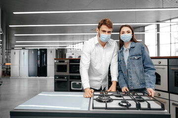 Young couple in medical masks looking at kitchen appliances in a mall