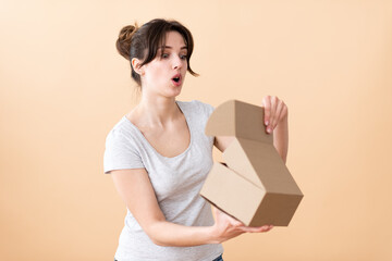 Girl surprised opening a cardboard box. Beige background