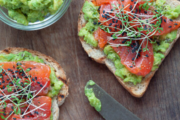Toasts with salted salmon fish, avocado and young sprouting greens on the wooden background, Close up	