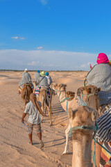 A caravan of people on camels moves through the sands of the Sahara Desert