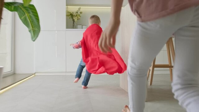 Little boy runs away from his sister. Boy is having fun playing with his sister running around apartment. Child superhero runs around the apartment running away from his sister in slow motion video.