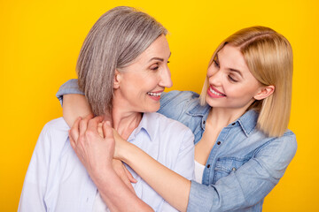 Obraz na płótnie Canvas Photo portrait of mother and daughter embracing looking on each other holding hands isolated vibrant yellow color background