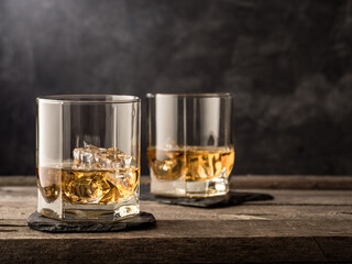 Two glasses of whiskey stand on an old wooden table. Copy space.
