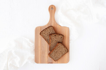 Slices of rye bread on a wooden cutting board on a white napkin and textured background