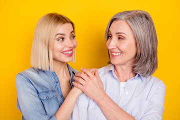 Photo portrait of daughter and mother smiling holding hands looking on each other isolated bright yellow color background