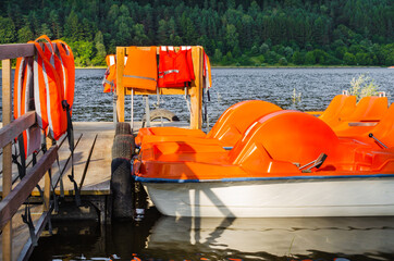 Orange catamarans on lake moored at the pier. Pleasure boats with life jackets.