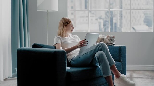 Cheerful woman works on tablet near meowing cat on couch