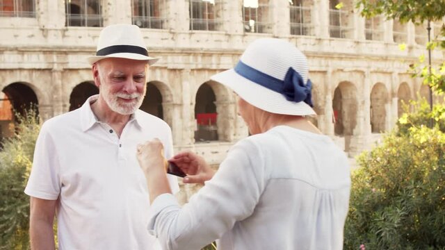 Family of senior travelers enjoy vacation in Rome. Senior couple make photo on phone near Colosseum
