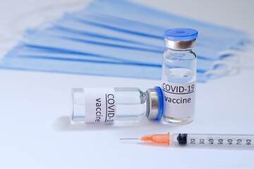 Creative ideas of vaccination concept. Top view of syringe with medical masks and vaccine vial glass bottles for vaccination against COVID-19. Coronavirus pandemic. Copy space. 