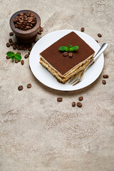 Portion of Traditional Italian Tiramisu dessert and coffee beans on grey concrete background