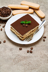 Portion of Traditional Italian Tiramisu dessert and coffee beans on grey concrete background
