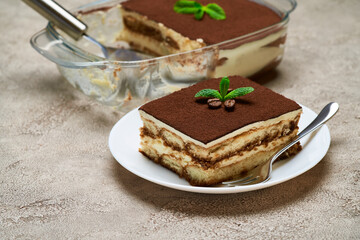 Traditional Italian Tiramisu dessert in glass baking dish and portion on grey concrete background