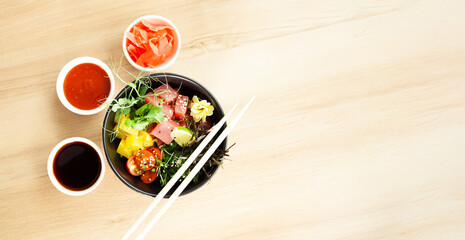 Poke salad with tuna in a bowl. Ingredients fresh tuna, cherry tomatoes, marinated seaweed, rice, takuan, Ponzu sauce, Teriyaki sauce, nori, sesame seeds, lime, cilantro. Asian seafood salad concept.