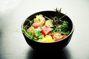 Poke salad with tuna in a bowl. Ingredients fresh tuna, cherry tomatoes, marinated seaweed, rice, takuan, Ponzu sauce, Teriyaki sauce, nori, sesame seeds, lime, cilantro. Asian seafood salad concept.