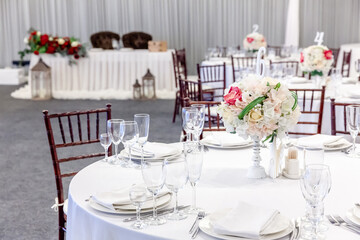 Fancy table set for dinner with flower composition in restaurant, luxury interior background. Wedding elegant banquet decoration and items for food arranged by catering service on white table.