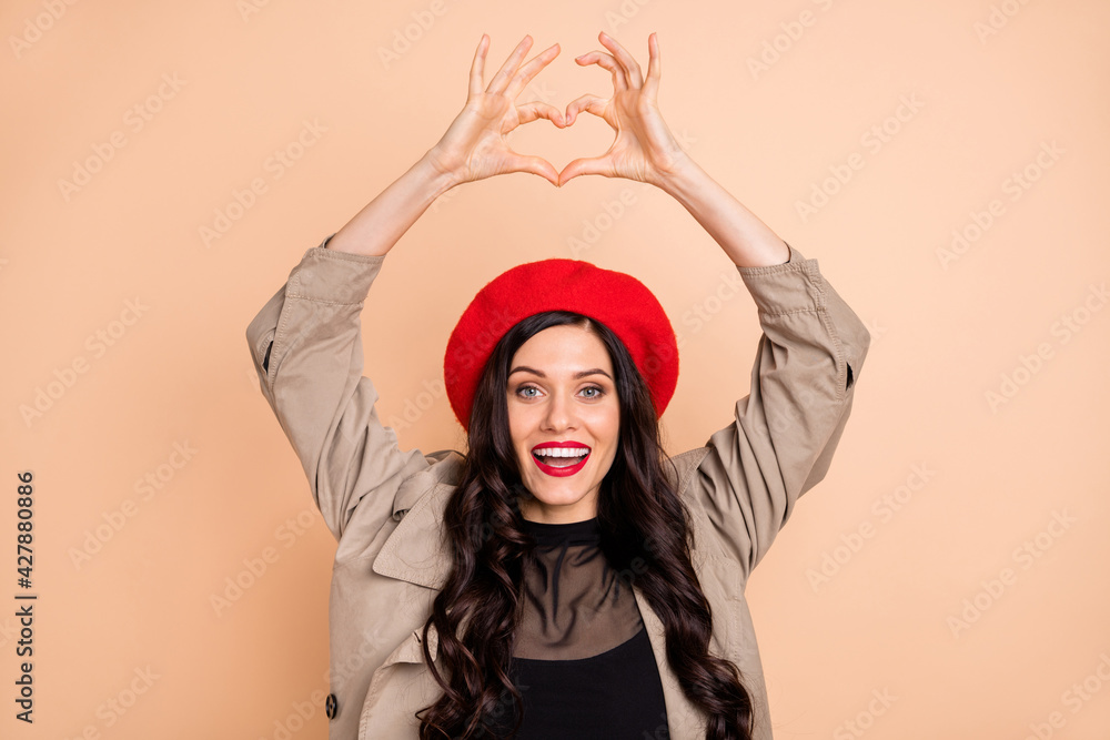 Sticker Photo of joyful lovely young woman make fingers heart shape above head isolated on beige color background