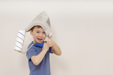 charming cute little emotional 5-year-old boy in a newspaper hat holds a white roller in his hand and shows the class . concept of apartment house (renovation)