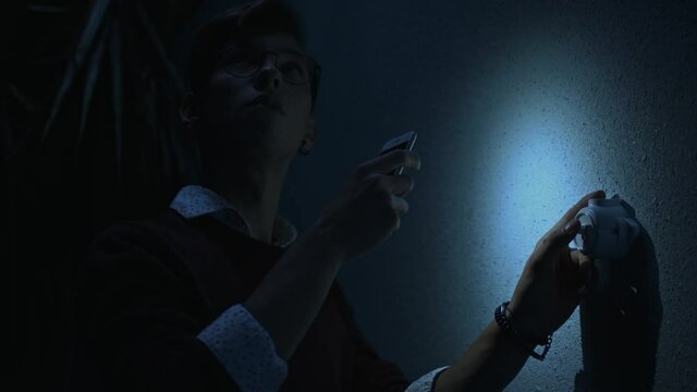 Young man with turned on mobile phone flash fails to turn on the light. Stock footage. Man turning on and off a switcher on the wall in a dark room, blackout concept.