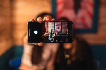 Dos amigas tomándose selfies en un bar decorado con temática circense