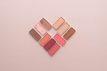 Eye shadow make up palette on a beige background. Heart shape created from cosmetics. Love and favorites beauty products concept.