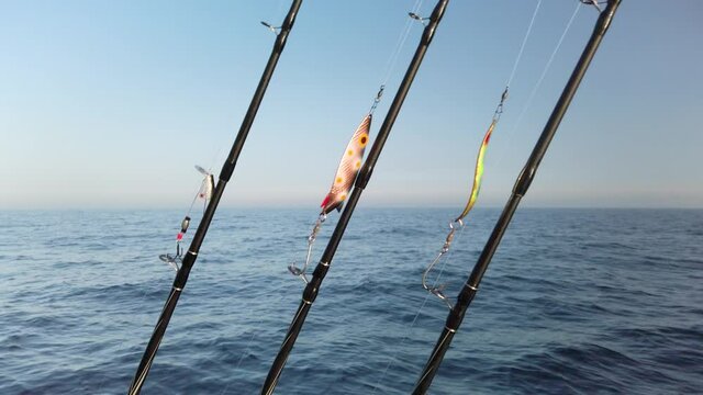 Three fishing rods hooked up with spinners, ready for fishing. The rods are lined up in a row on a small fishing boat. It is a beautiful sunny spring day. Slow motion 4K