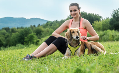 Woman runner and dog on field under golden sunset sky in evening time. Outdoor running. Athletic young man with his dog are running in nature.